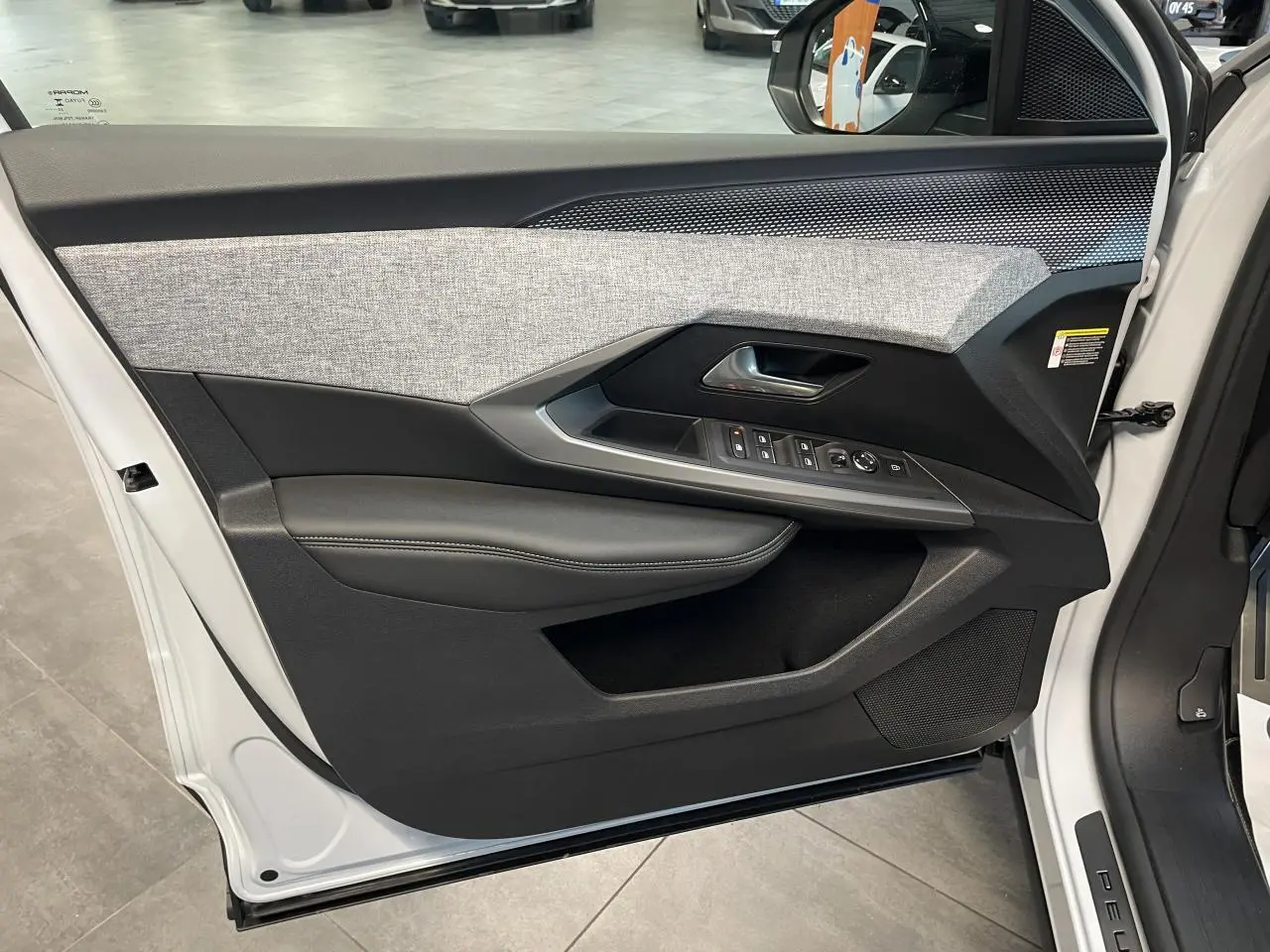 Vue intérieure de la porte avant gauche du Peugeot 3008 blanc Okenite avec habillage tissu gris et inserts noirs laqués.