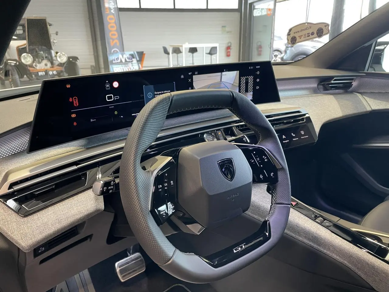 Vue intérieure du volant compact GT et du tableau de bord numérique du Peugeot 3008 Hybrid blanc Okenite.