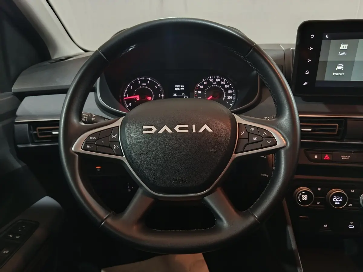 Vue rapprochée du volant en cuir noir de la Dacia Sandero 2024 avec commandes multifonctions et tableau de bord digital.