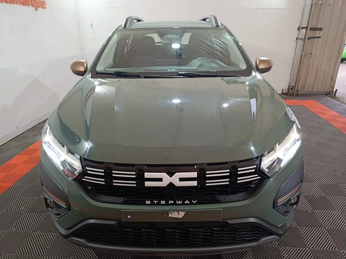 Vue avant rapprochée d'une Dacia Sandero Extreme+ TCe 110 2024 vert avec calandre noire et rétroviseurs cuivrés.