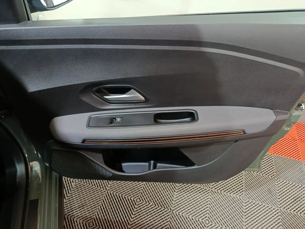 Vue intérieure côté gauche de la porte avant d’une Dacia Sandero Extreme+ TCe 110 2024 verte, avec poignée argentée et commande de vitre.