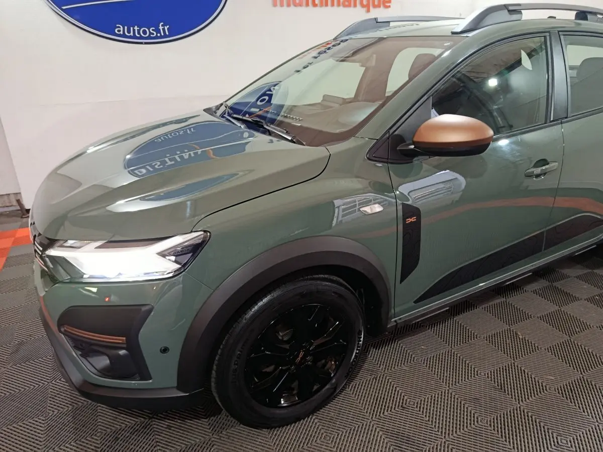 Vue 3/4 avant droit d'une Dacia Sandero Extreme+ 2024 vert avec rétroviseurs cuivrés et jantes noires brillantes.