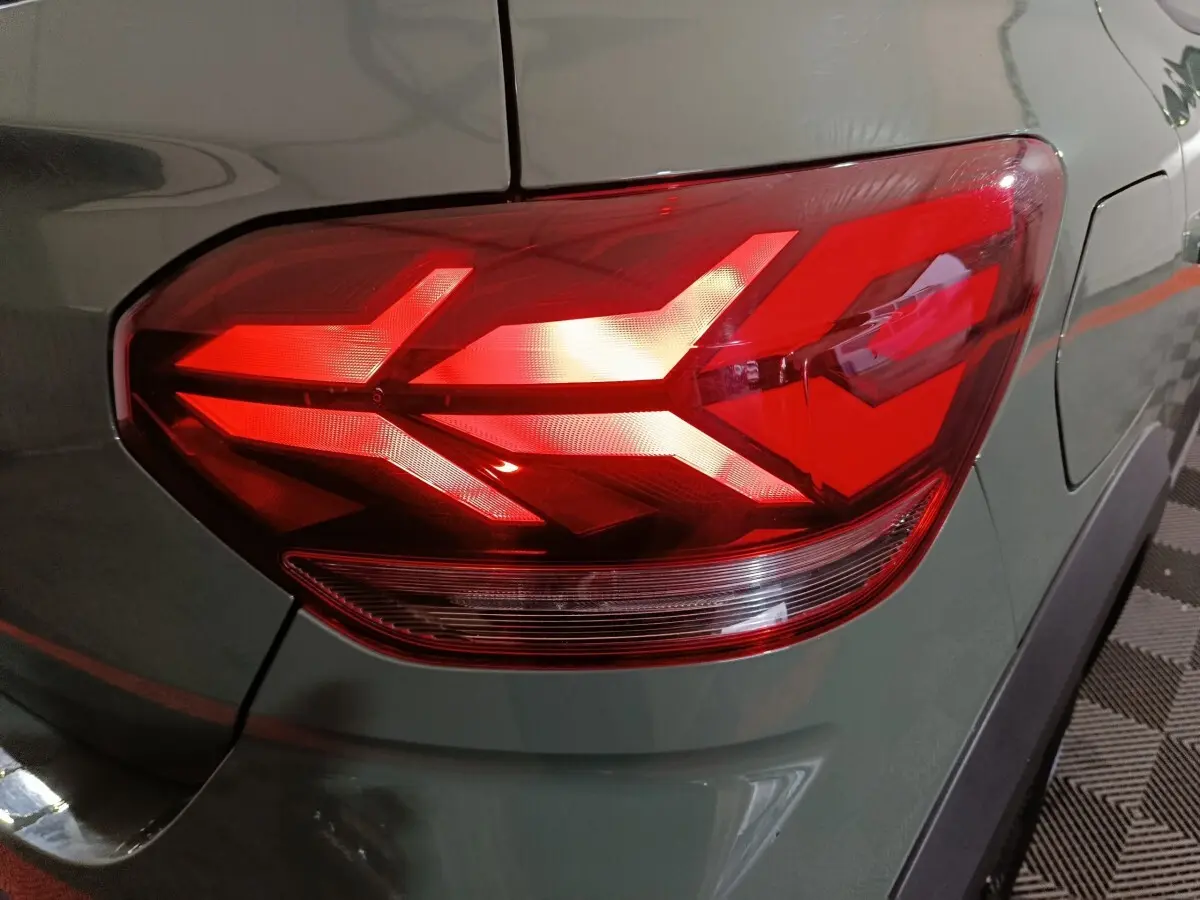 Gros plan sur le feu arrière droit rouge vif d'une Dacia Sandero Extreme+ vert 2024, avec carrosserie et pare-chocs visibles.