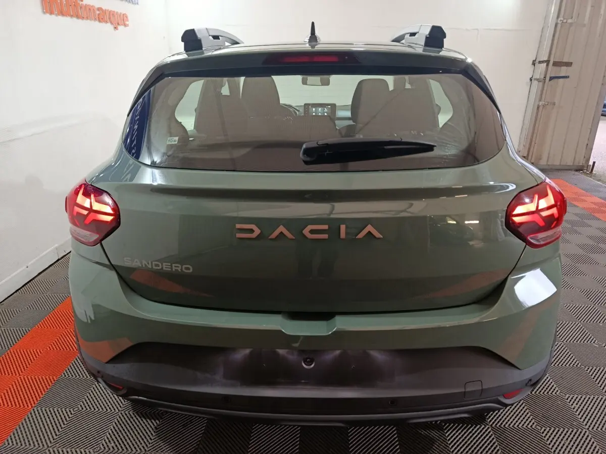 Vue arrière d'une Dacia Sandero Extreme+ TCe 110 2024 en vert avec feux LED allumés et barres de toit noires.