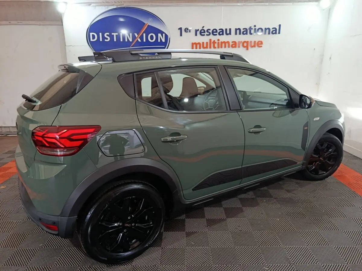 Vue 3/4 arrière droite d'une Dacia Sandero Extreme+ 2024 verte avec jantes noires et rails de toit assortis.