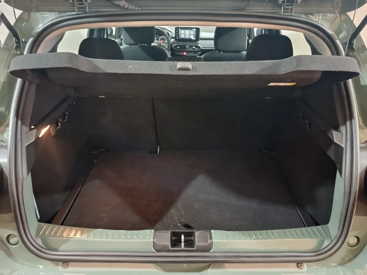 Coffre ouvert vu de l'arrière d'une Dacia Sandero Extreme+ TCe 110 vert, intérieur noir et tablette de coffre relevée.