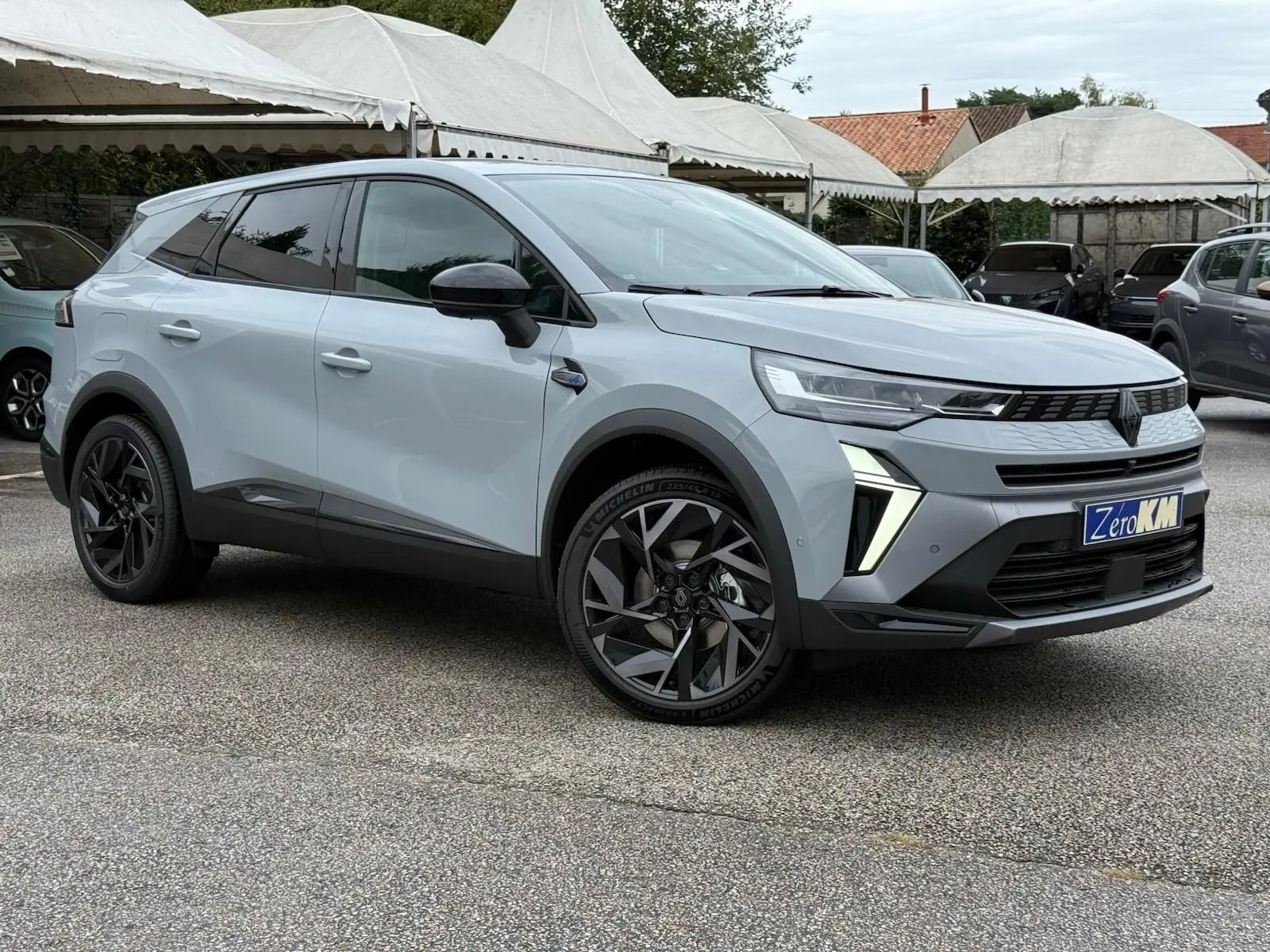 Renault Symbioz gris Rafale en vue 3/4 avant droit, avec jantes noires et feux LED distinctifs allumés.