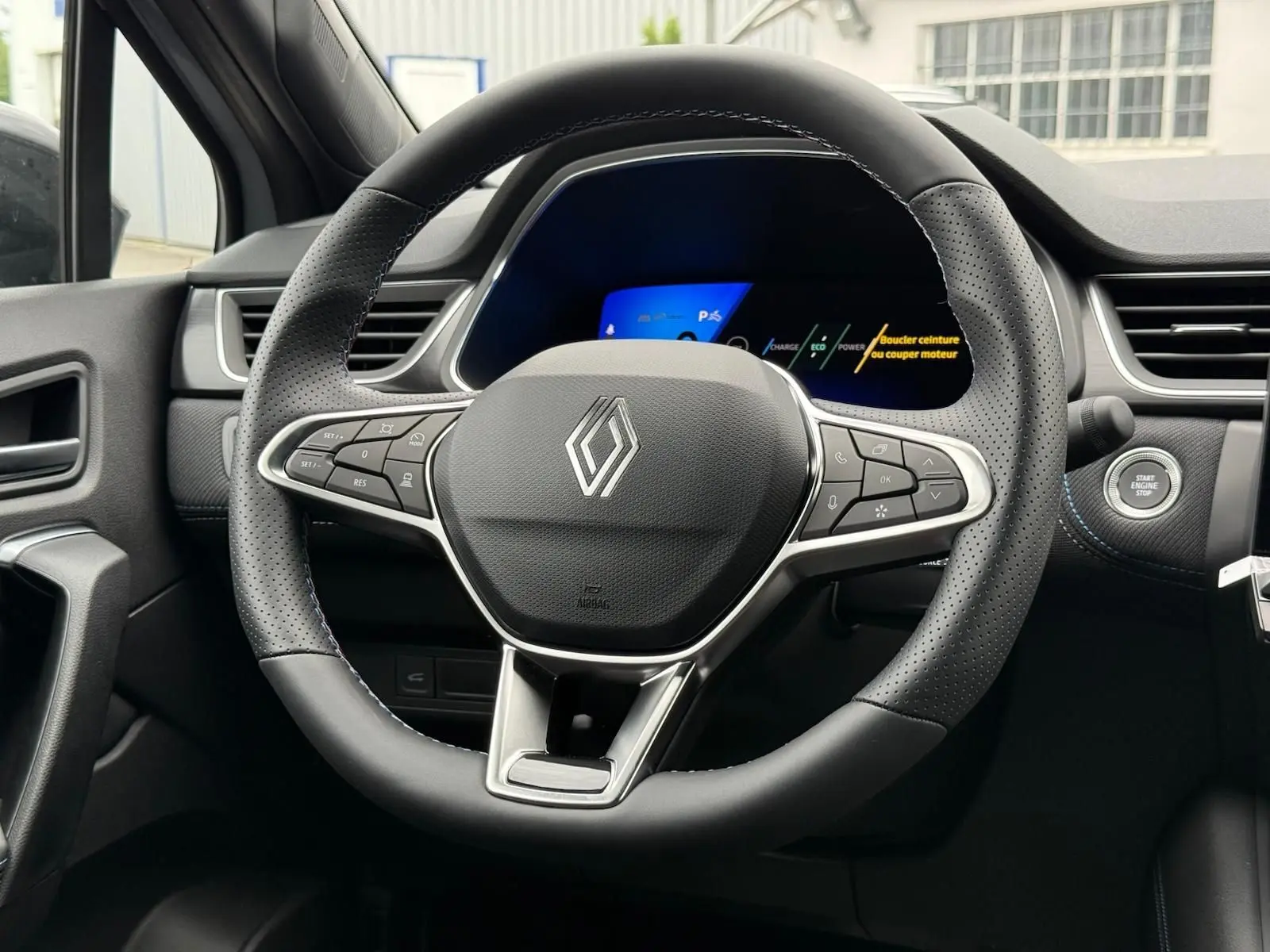 Vue rapprochée du volant noir perforé de la Renault Symbioz 2026 avec tableau de bord digital et bouton Start/Stop.