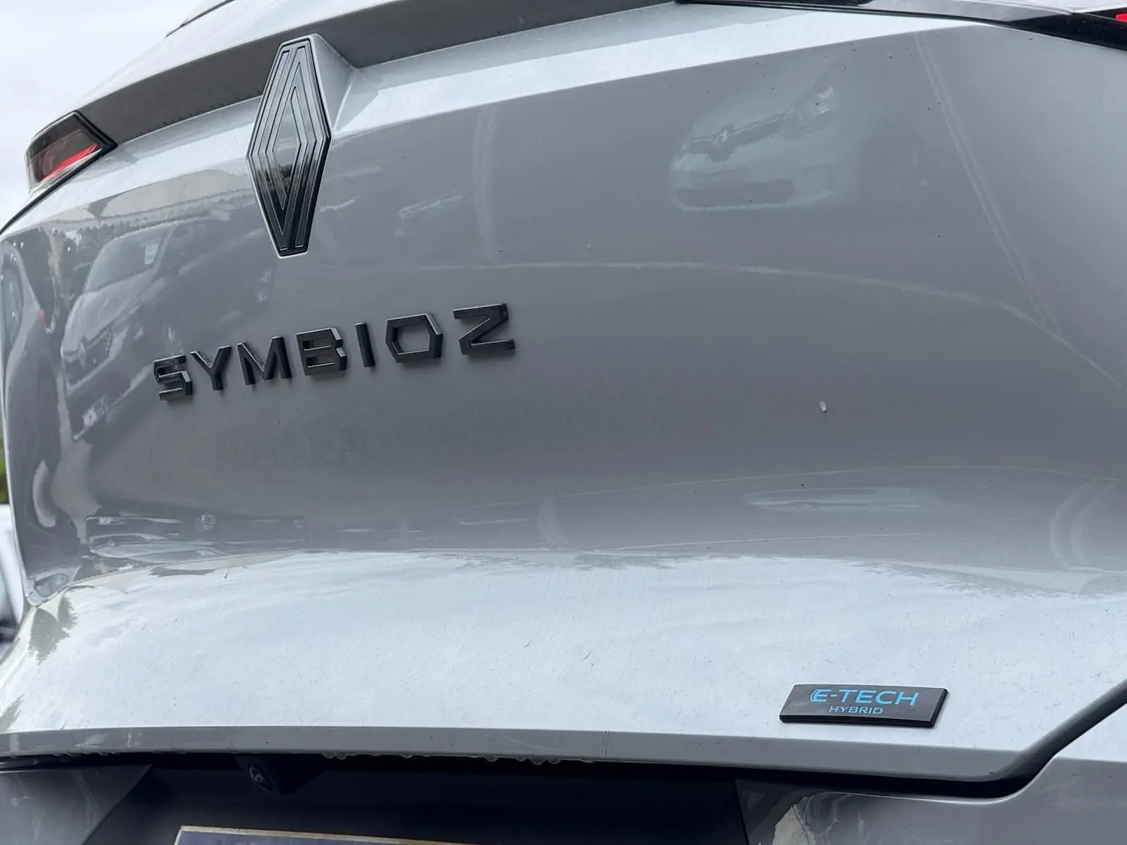 Gros plan arrière du Renault Symbioz gris Rafale avec logo et badge E-TECH Hybrid visibles sur le coffre.