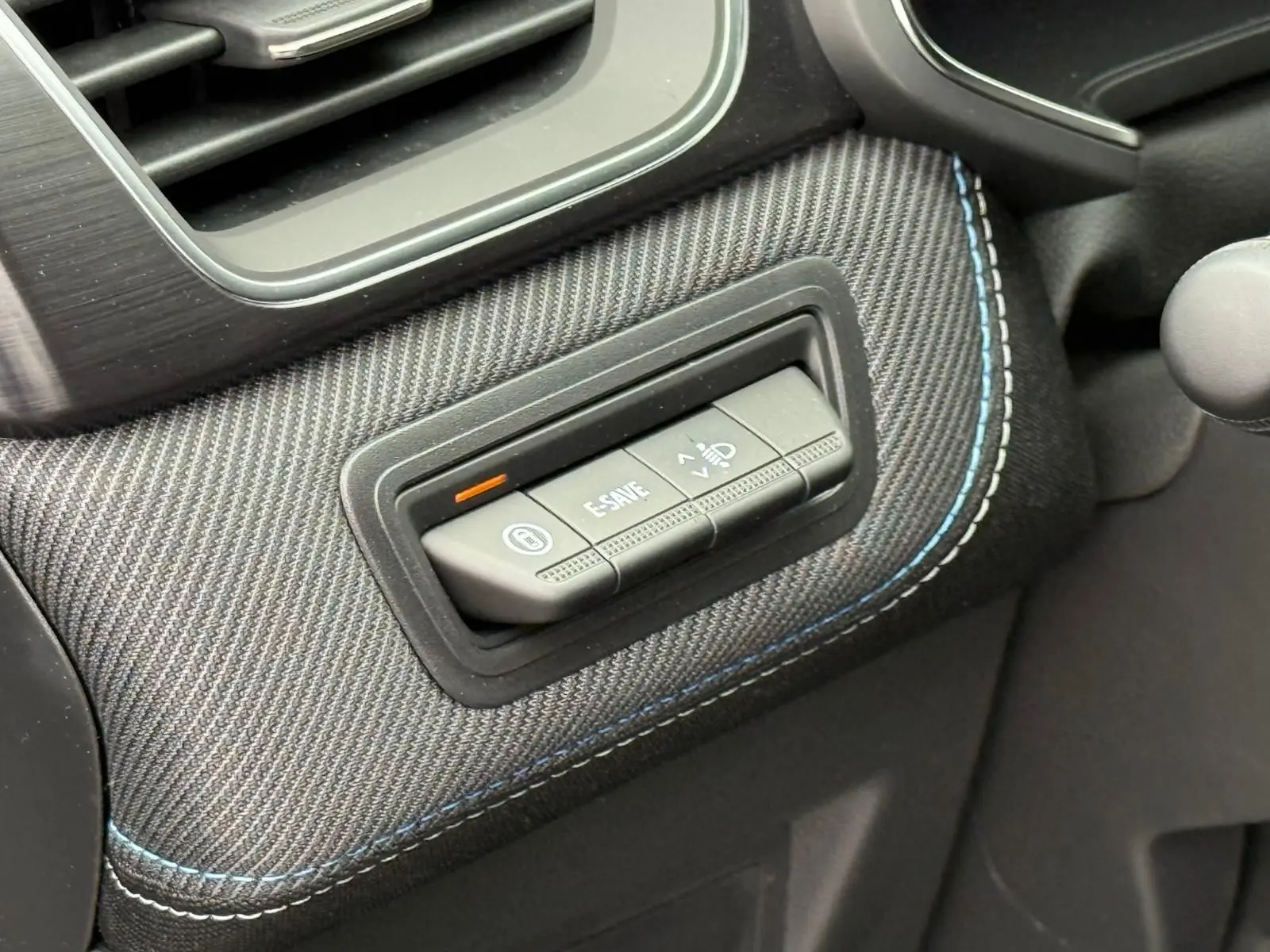 Détail intérieur montrant les boutons de commande sur une garniture en tissu gris avec surpiqûres bleues du Renault Symbioz 2026.