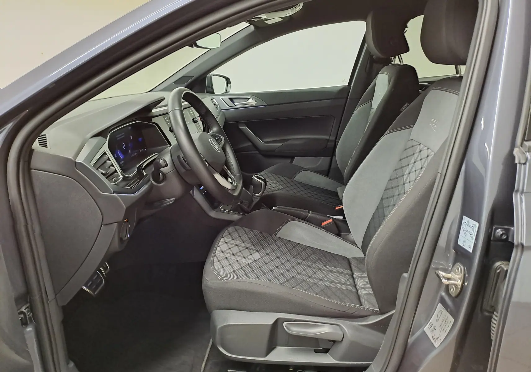 Vue intérieure côté conducteur d'une Volkswagen Polo gris cendré 2025, sièges tissu avec surpiqûres et volant multifonction.