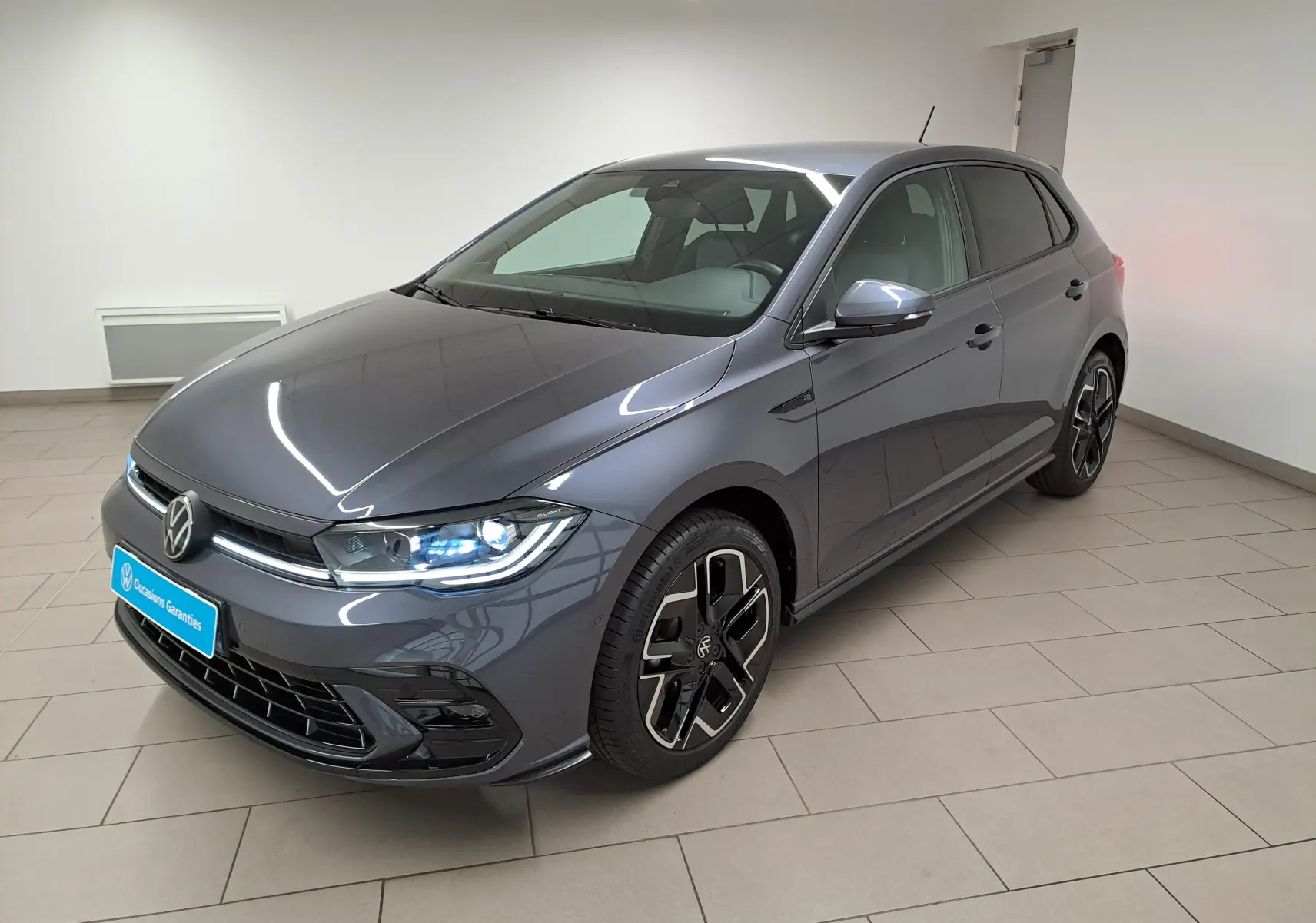 Volkswagen Polo 1.0 TSI R-Line gris cendré vue 3/4 avant avec phares allumés et jantes noires distinctives.