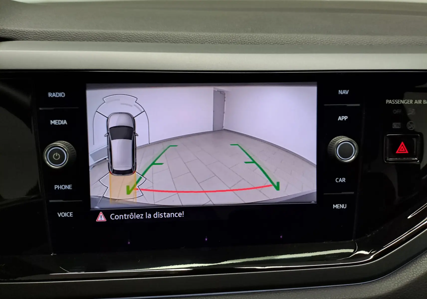 Écran de caméra de recul affichant une Volkswagen Polo gris cendré en vue aérienne avec guidage de trajectoire verte et rouge.