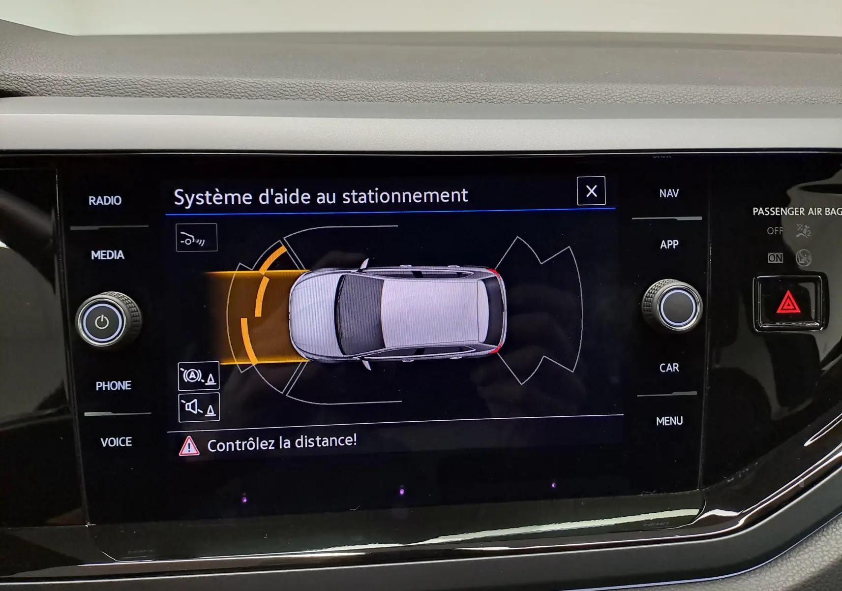 Écran du système d'aide au stationnement affichant une vue aérienne du véhicule gris cendré avec alertes de proximité.