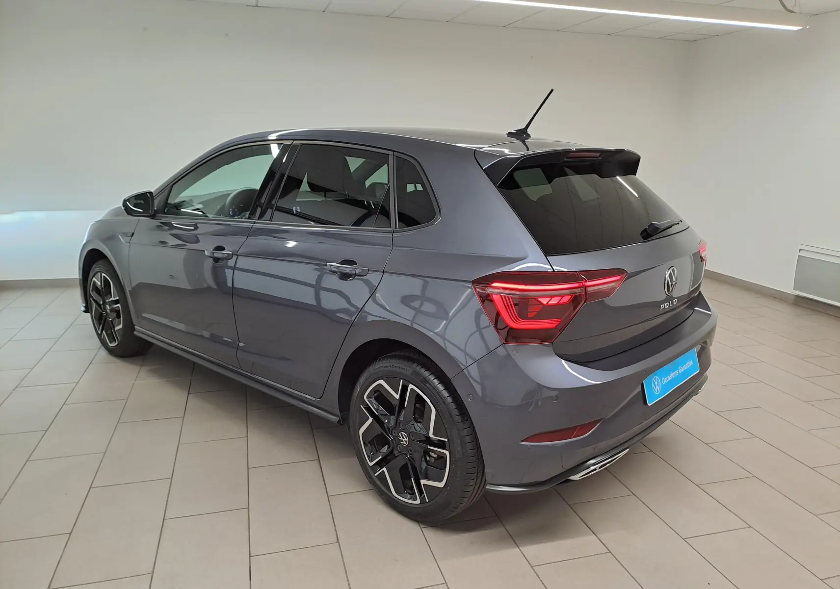 Volkswagen Polo 1.0 TSI R-Line gris cendré vue 3/4 arrière droit en intérieur avec jantes noires et rouges.
