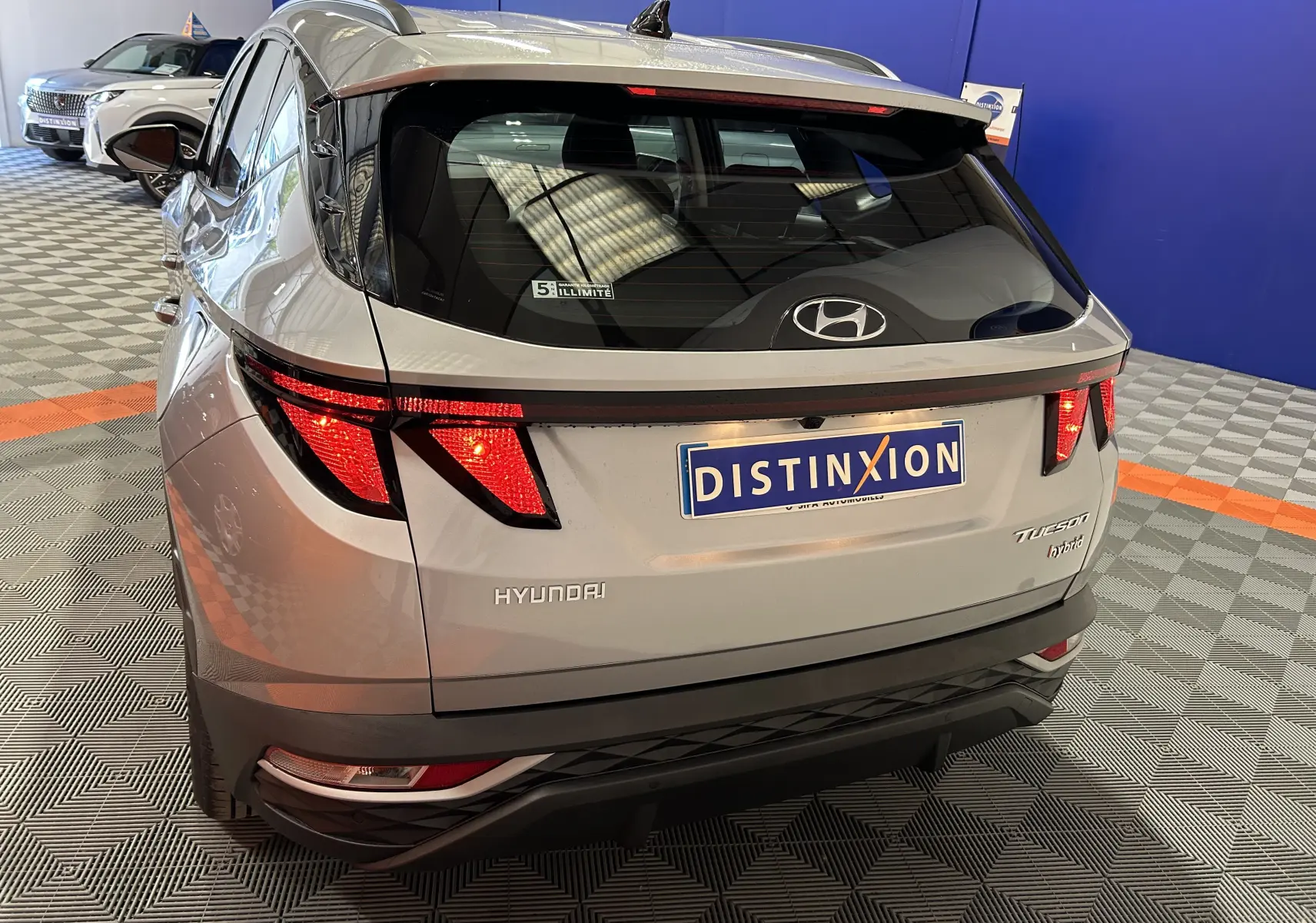 Vue 3/4 arrière droite d'un Hyundai Tucson hybride gris Shimmering Metal avec feux arrière allumés en showroom.