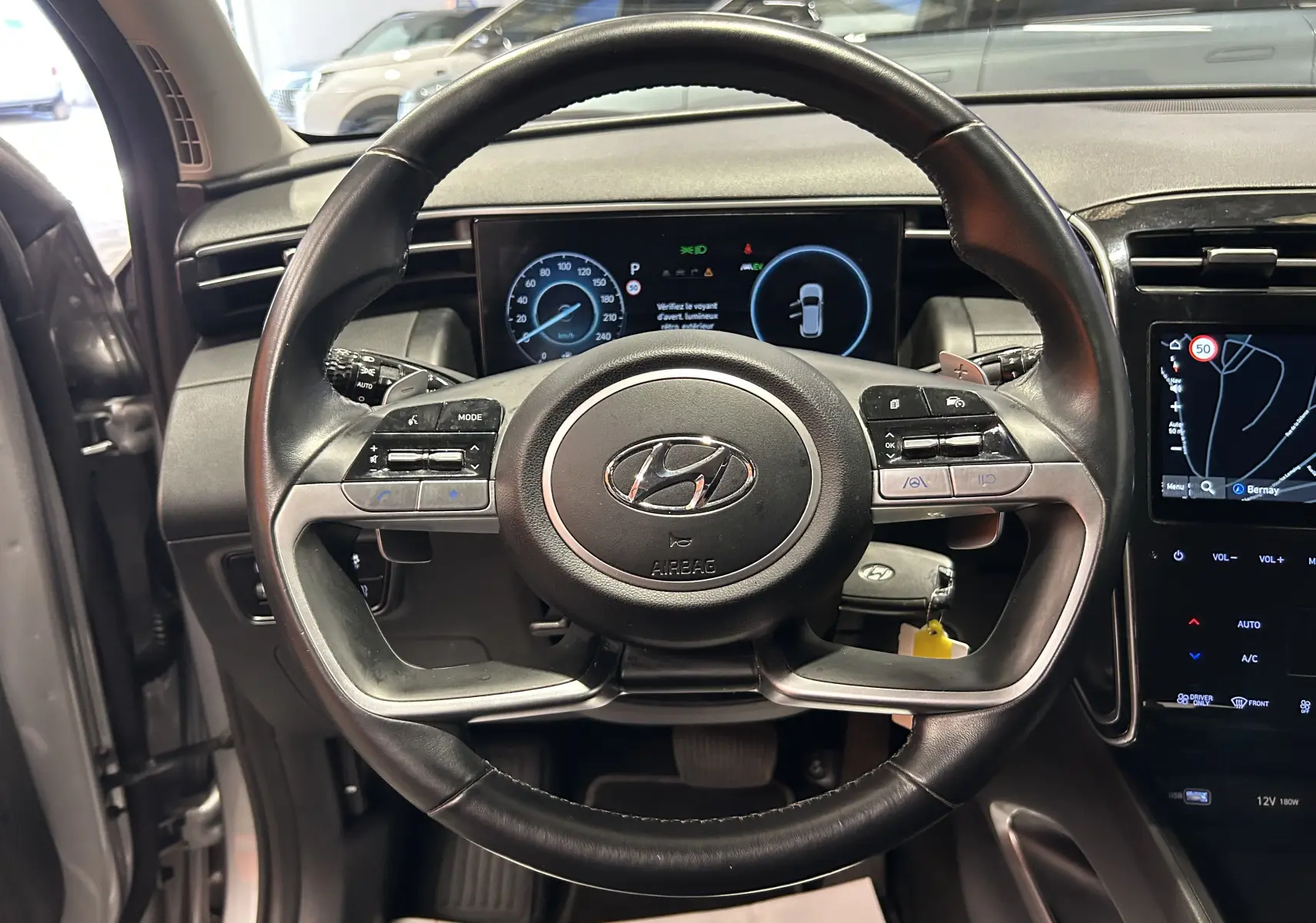 Vue intérieure centrée sur le volant cuir noir du Hyundai Tucson Hybrid 2022 avec tableau de bord numérique et écran GPS.