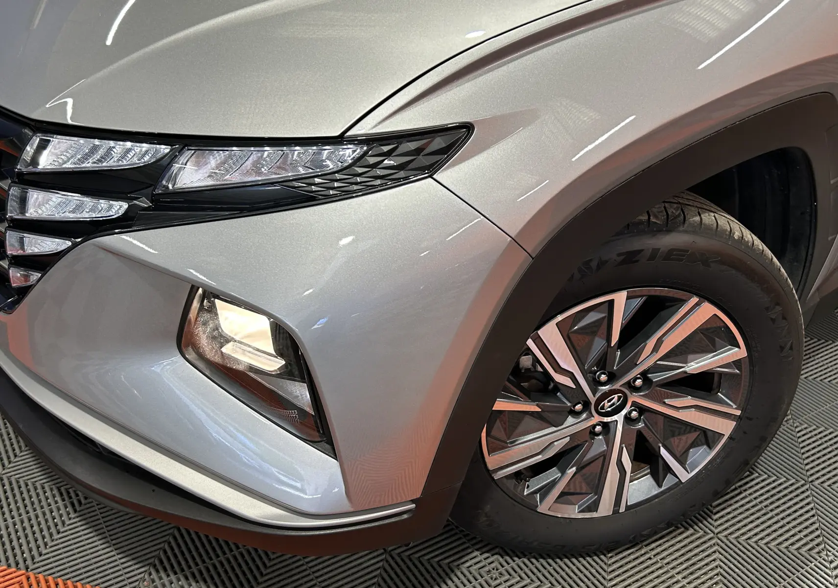 Gros plan sur l’avant droit gris Shimmering Metal du Hyundai Tucson Hybrid, mettant en valeur le phare et la roue alliage.