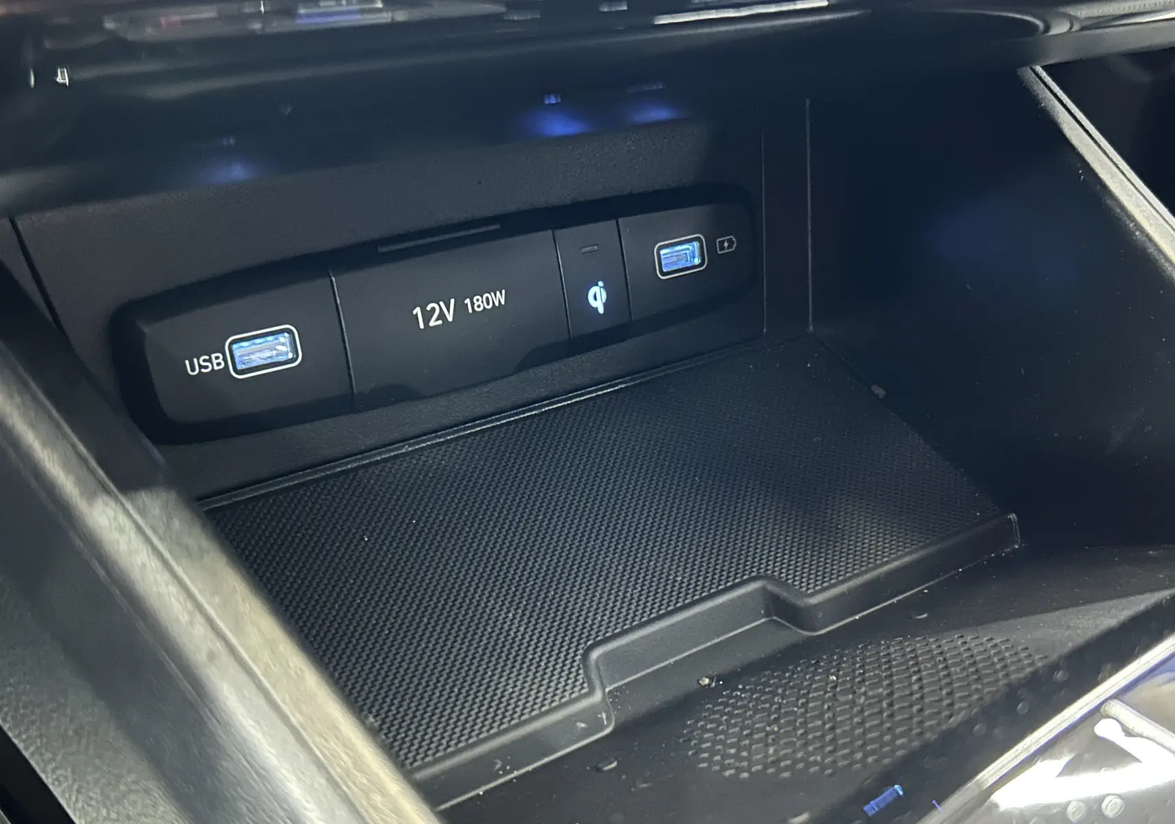 Gros plan sur la console centrale noire du Hyundai Tucson Hybrid 2022, montrant ports USB, prise 12V et chargeur sans fil Qi.