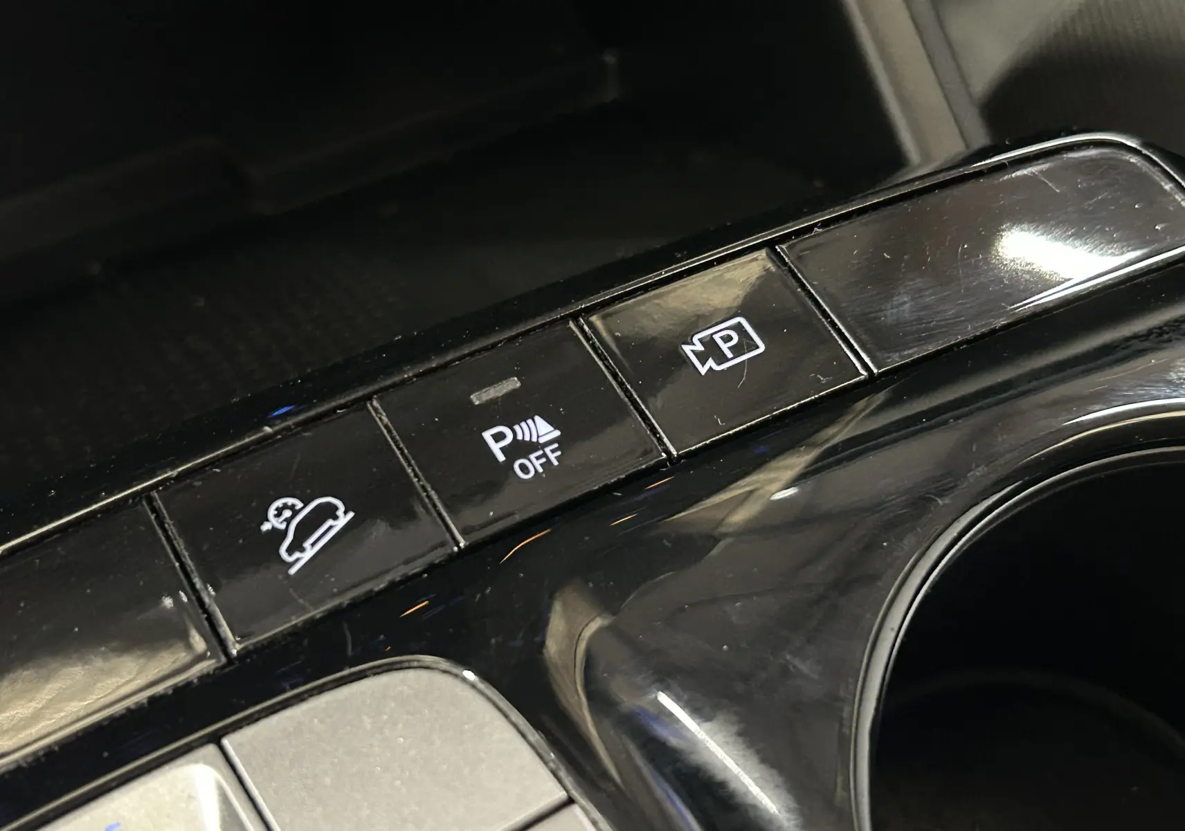 Gros plan sur les boutons de commande du système d’aide au stationnement et caméra dans l’habitacle noir du Hyundai Tucson gris.