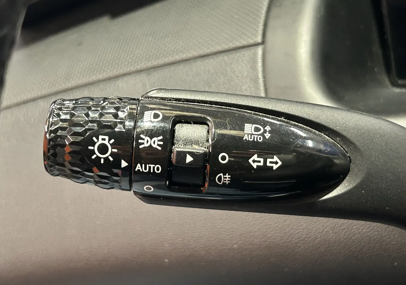 Gros plan sur la commande des phares et clignotants noire avec motifs texturés dans l'habitacle du Hyundai Tucson gris.