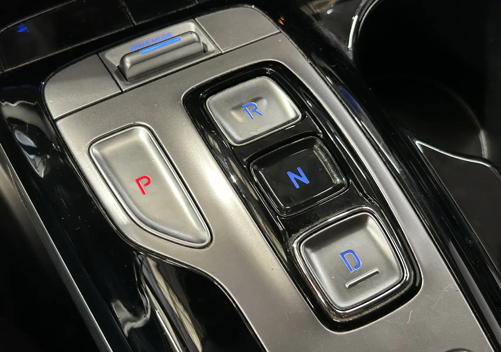 Gros plan sur la console centrale du Hyundai Tucson gris, montrant les boutons de la boîte automatique avec éclairage bleu et rouge.