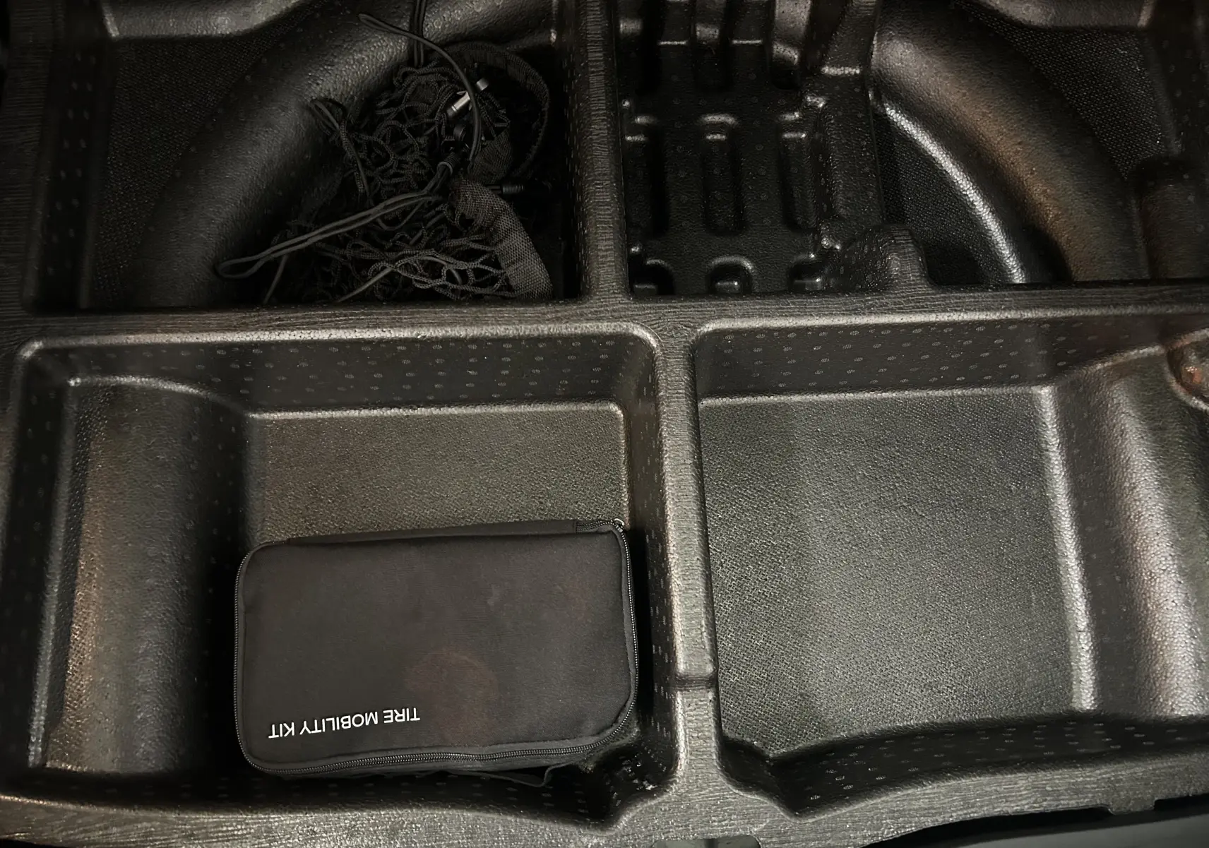 Rangement sous coffre du Hyundai Tucson gris, montrant un kit de mobilité pneu noir dans un compartiment en plastique.