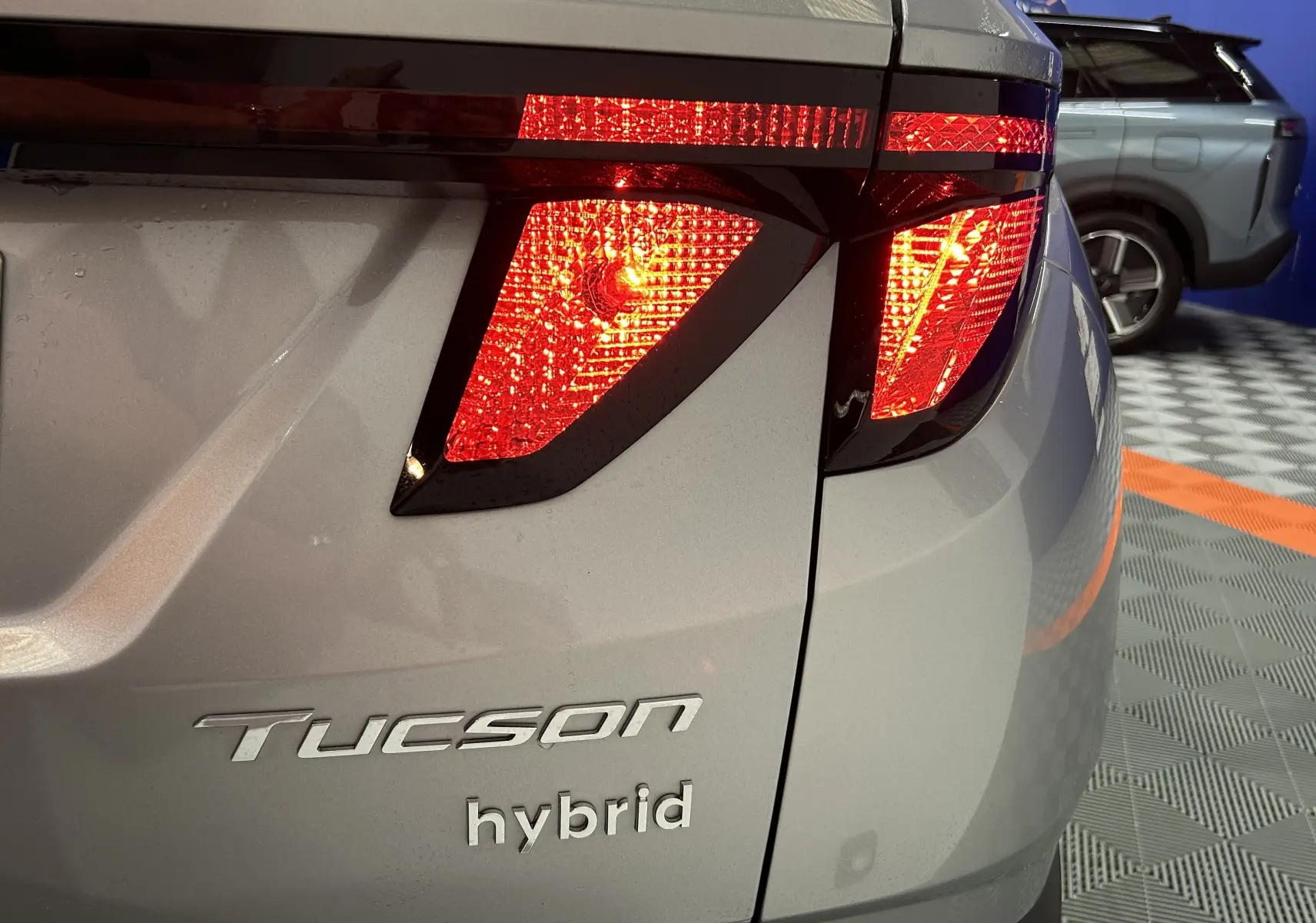 Gros plan sur le feu arrière droit allumé d'un Hyundai Tucson hybride gris Shimmering Metal, avec logo Tucson visible.