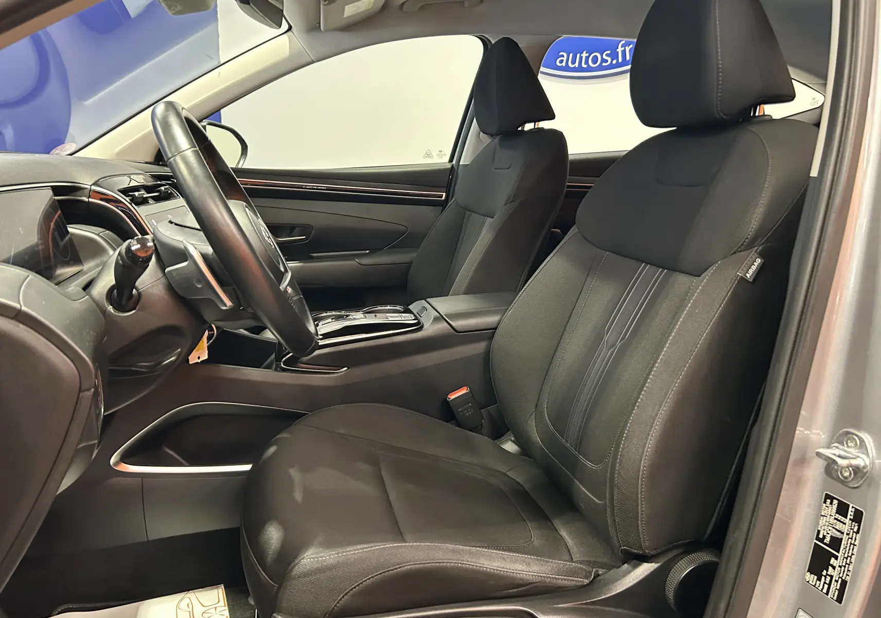 Vue intérieure côté conducteur du Hyundai Tucson hybride 2022, sièges tissu noir et tableau de bord moderne gris.
