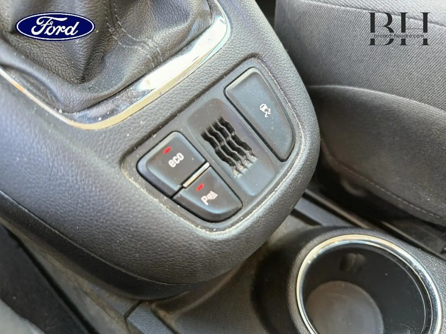 Gros plan sur la console centrale noire avec boutons Eco et aide au stationnement, volant cuir partiel visible.