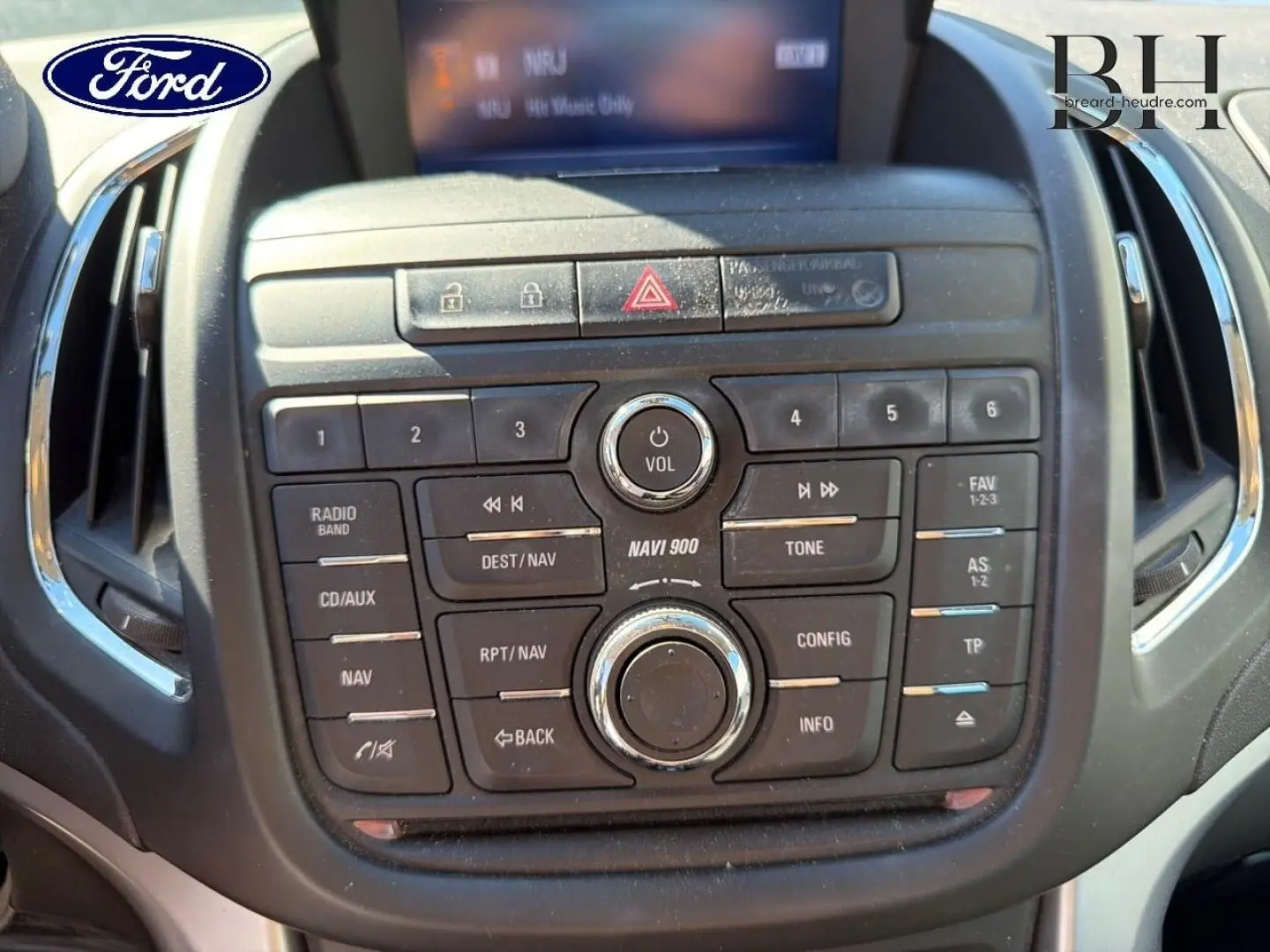 Console centrale noire vue de face avec commandes audio et navigation, affichage digital partiel, intérieur Ford.