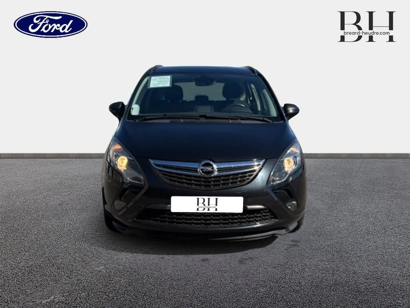 Vue avant d’un Opel Zafira Tourer gris métal avec phares allumés sur fond neutre.