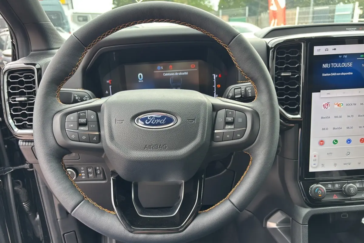 Volant en cuir noir avec surpiqûres orange du Ford Ranger 2025 Wildtrak Plus, tableau de bord et écran tactile visibles.