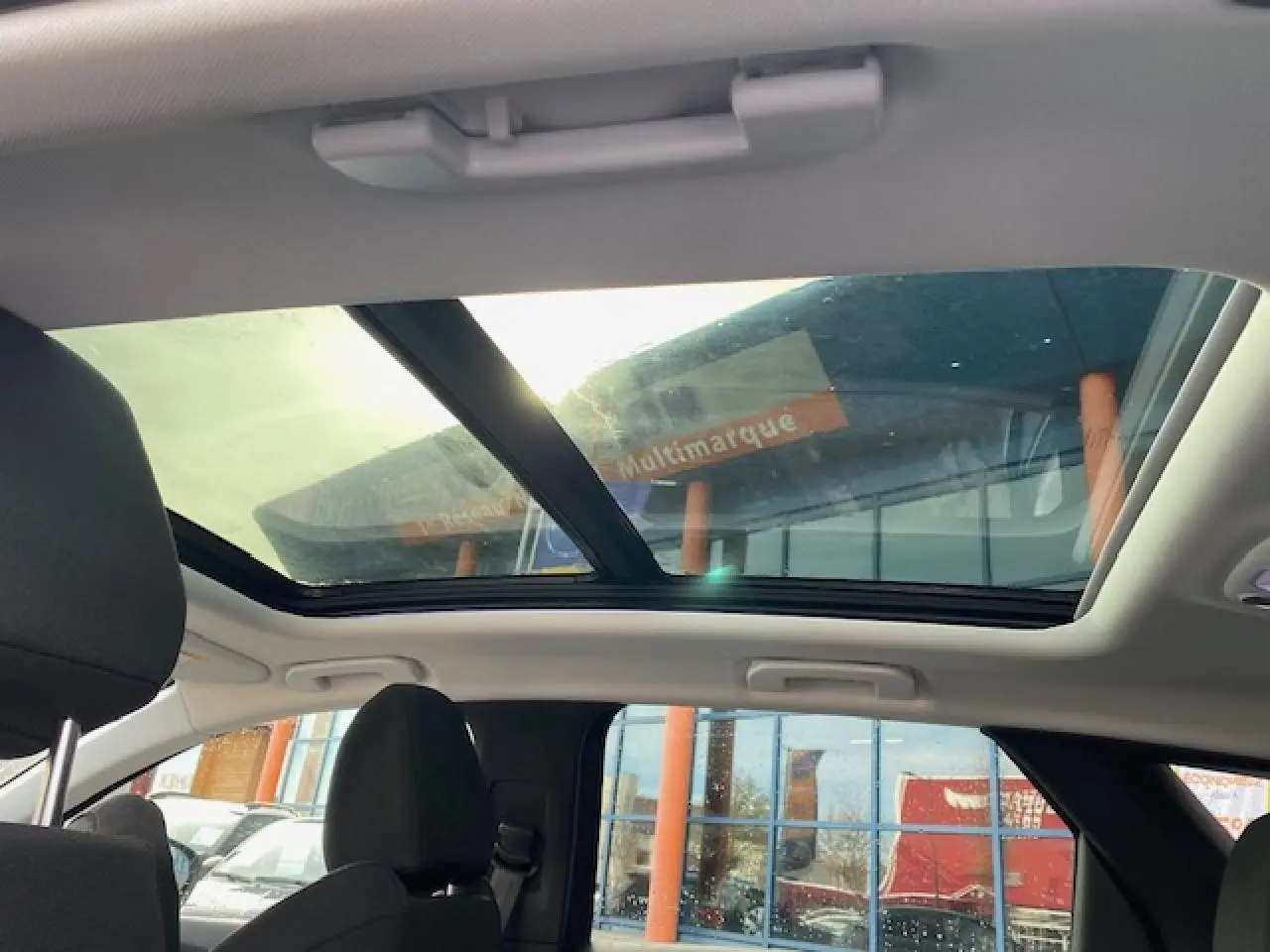 Toit ouvrant panoramique vu de l'intérieur arrière du Peugeot 3008 gris platinium avec sièges noirs et ciel de toit clair.