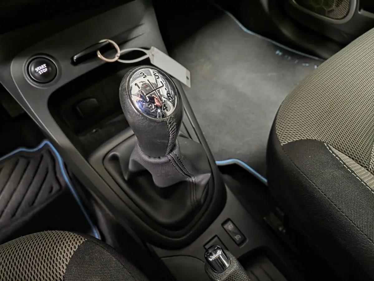 Gros plan sur le levier de vitesses manuel et siège avant gris clair ivoire du Renault Captur noir de 2014.