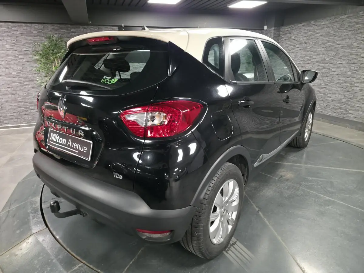 Vue 3/4 arrière droite d'un Renault Captur noir avec toit blanc, attelage et jantes alliage 16 pouces dans un garage.