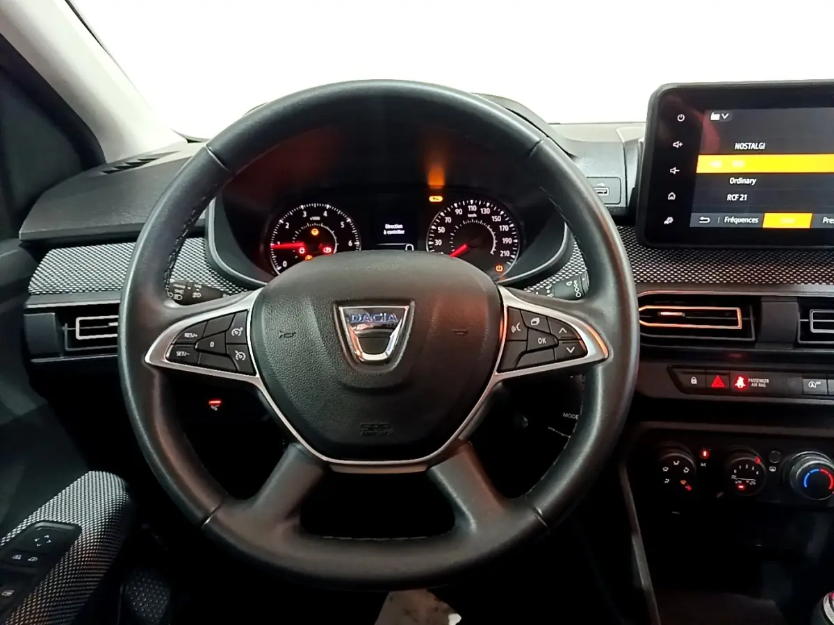 Vue intérieure centrée sur le volant cuir noir multifonctions de la Dacia Sandero blanc, avec tableau de bord et écran tactile.