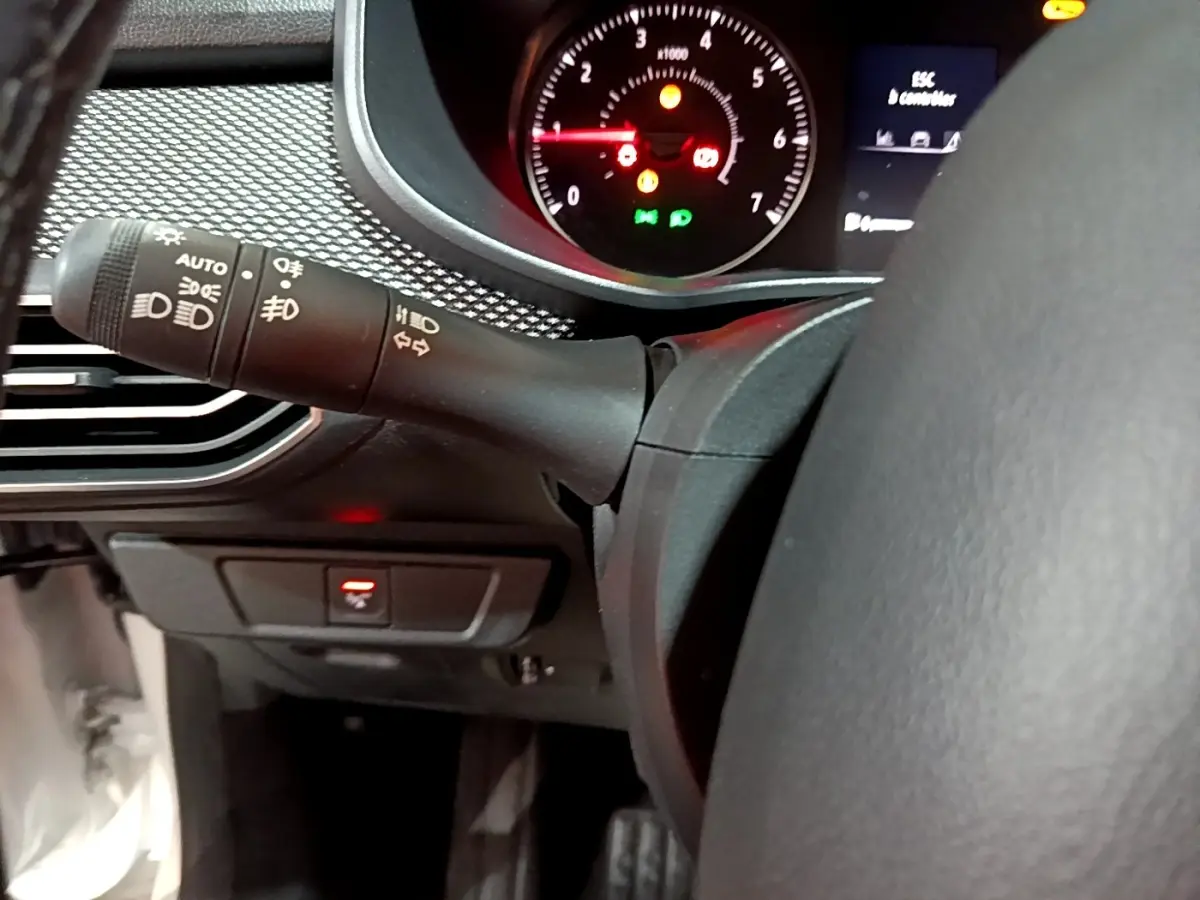 Gros plan intérieur sur le volant cuir synthétique et la commande des phares de la Dacia Sandero Confort TCe 90 blanche.