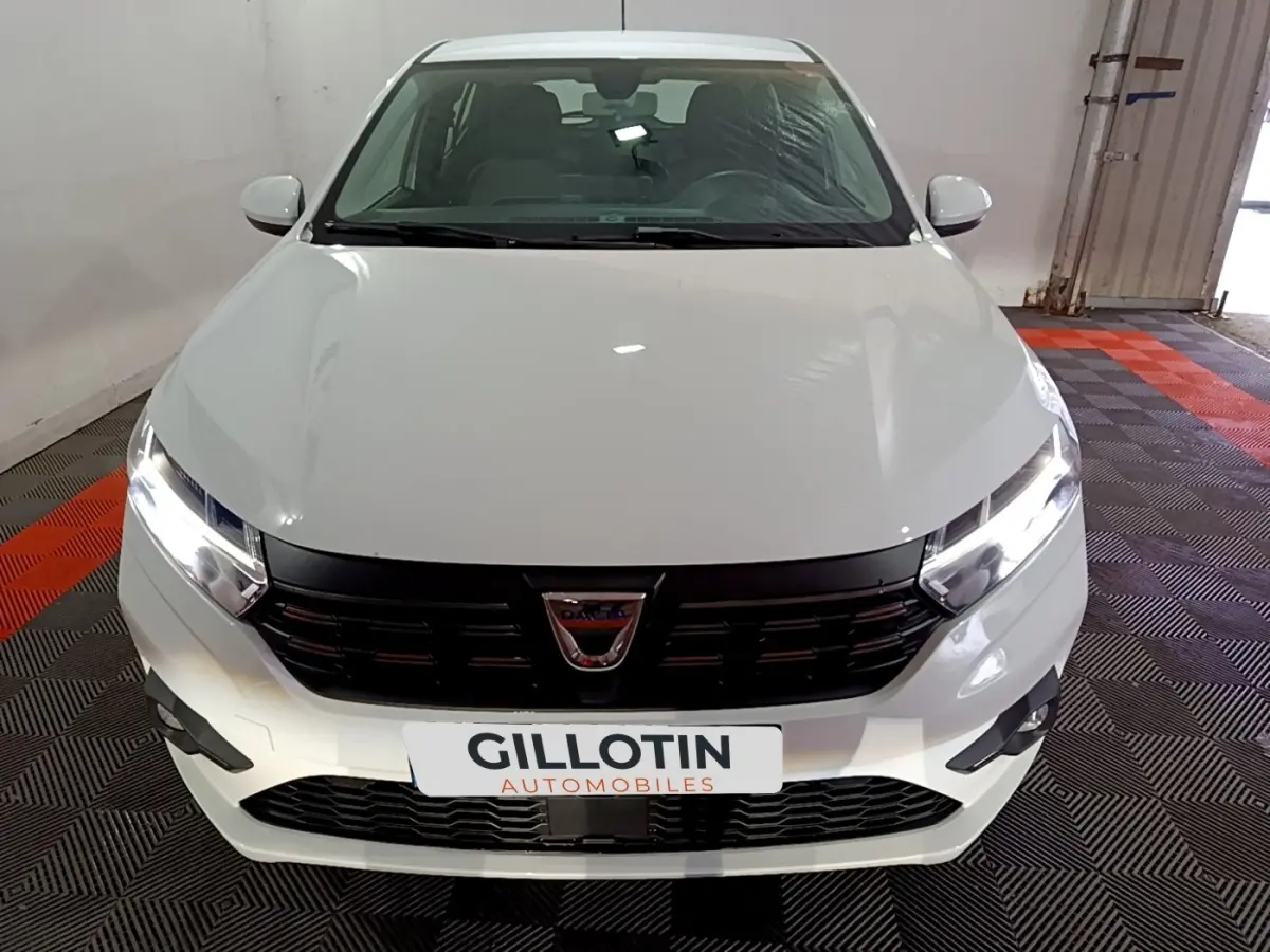 Vue frontale d'une Dacia Sandero blanche 2022 avec phares LED allumés et calandre noire brillante.