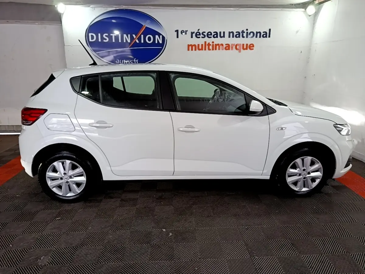 Vue de profil côté gauche d'une Dacia Sandero blanche 2022 dans un garage avec logo Distinxion en arrière-plan.