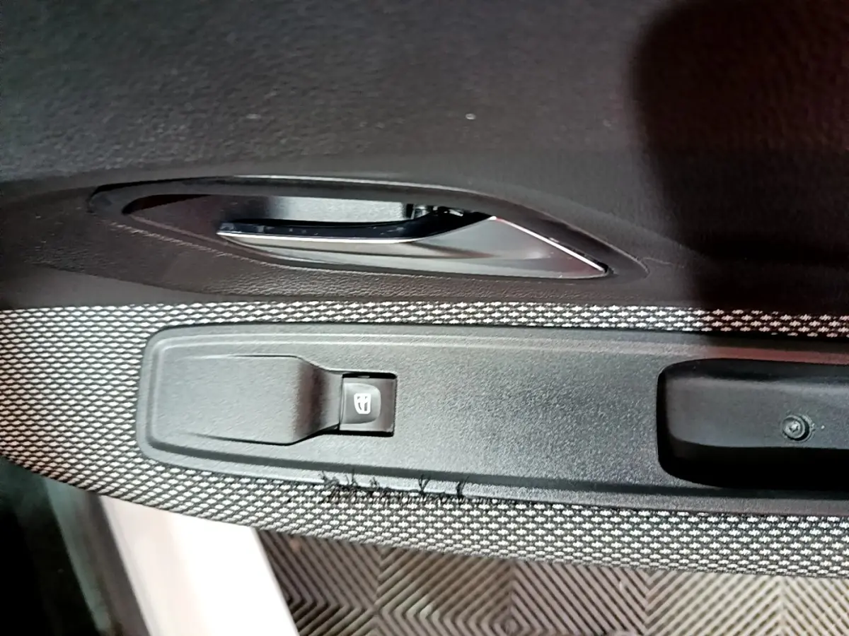 Gros plan sur la commande de lève-vitre côté conducteur d'une Dacia Sandero blanc, avec poignée de porte noire.