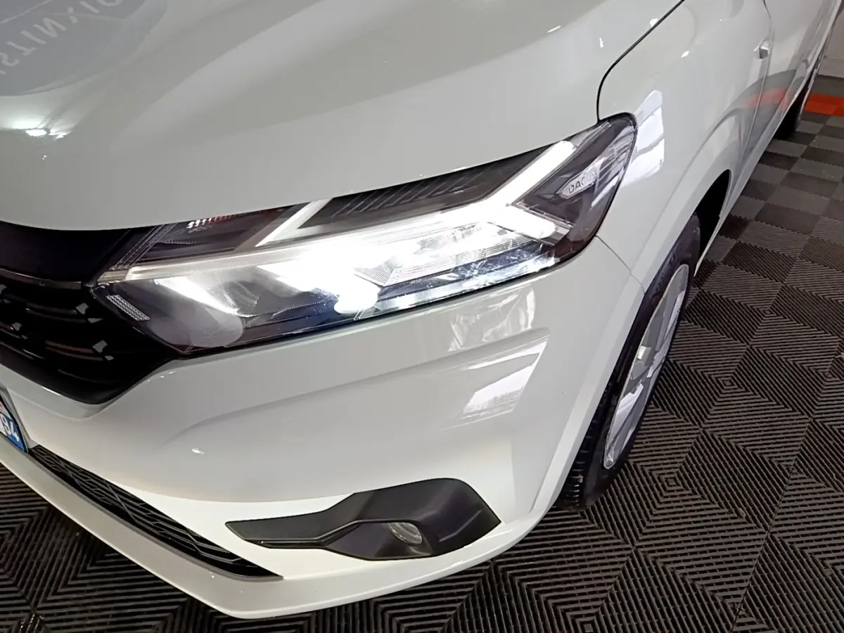 Gros plan sur l'avant droit blanc d'une Dacia Sandero 2022 avec phares LED allumés et antibrouillards visibles.