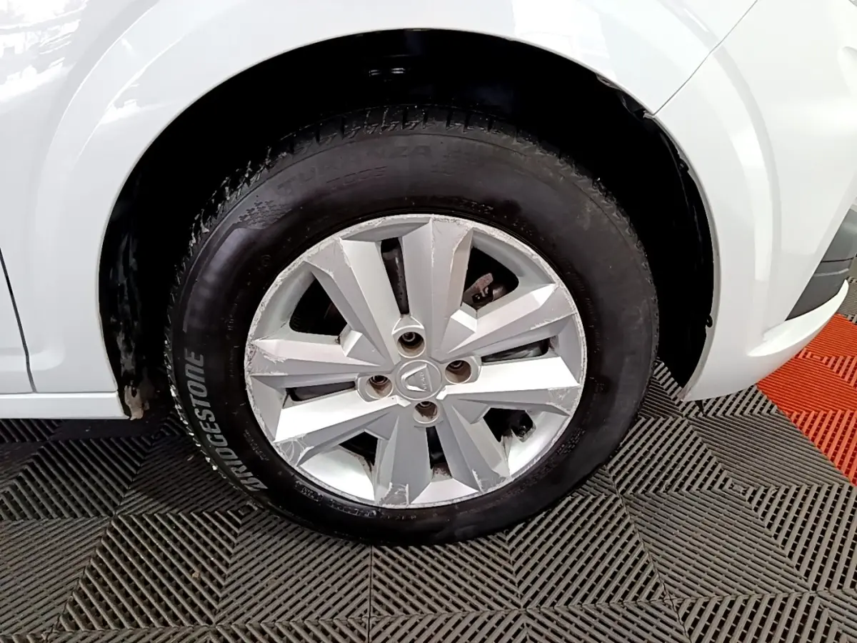 Gros plan sur la roue avant gauche d'une Dacia Sandero blanche, jante en alliage argentée avec pneus Bridgestone.