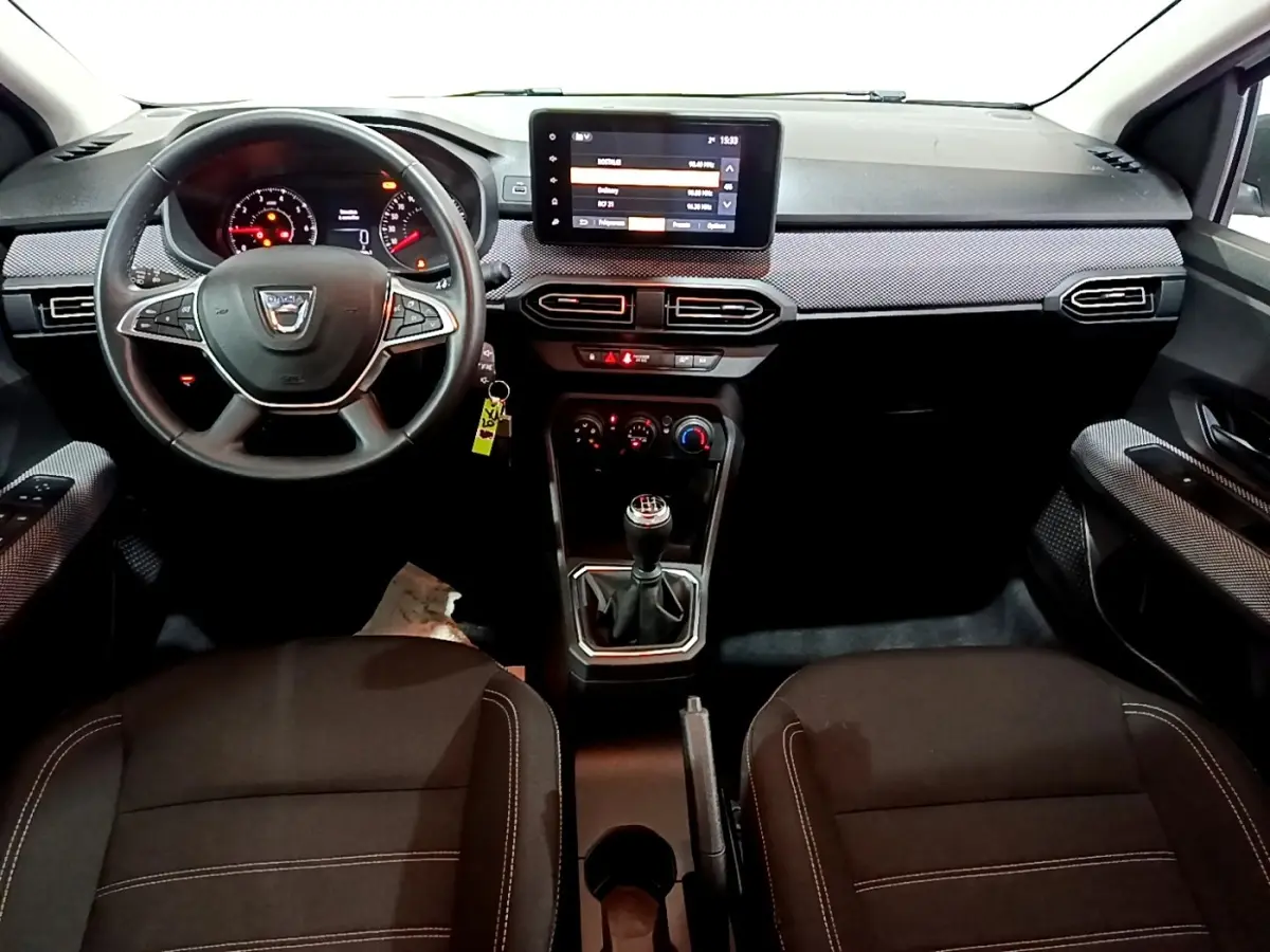 Vue intérieure avant centrée sur le tableau de bord et volant cuir synthétique de la Dacia Sandero Confort 2022.