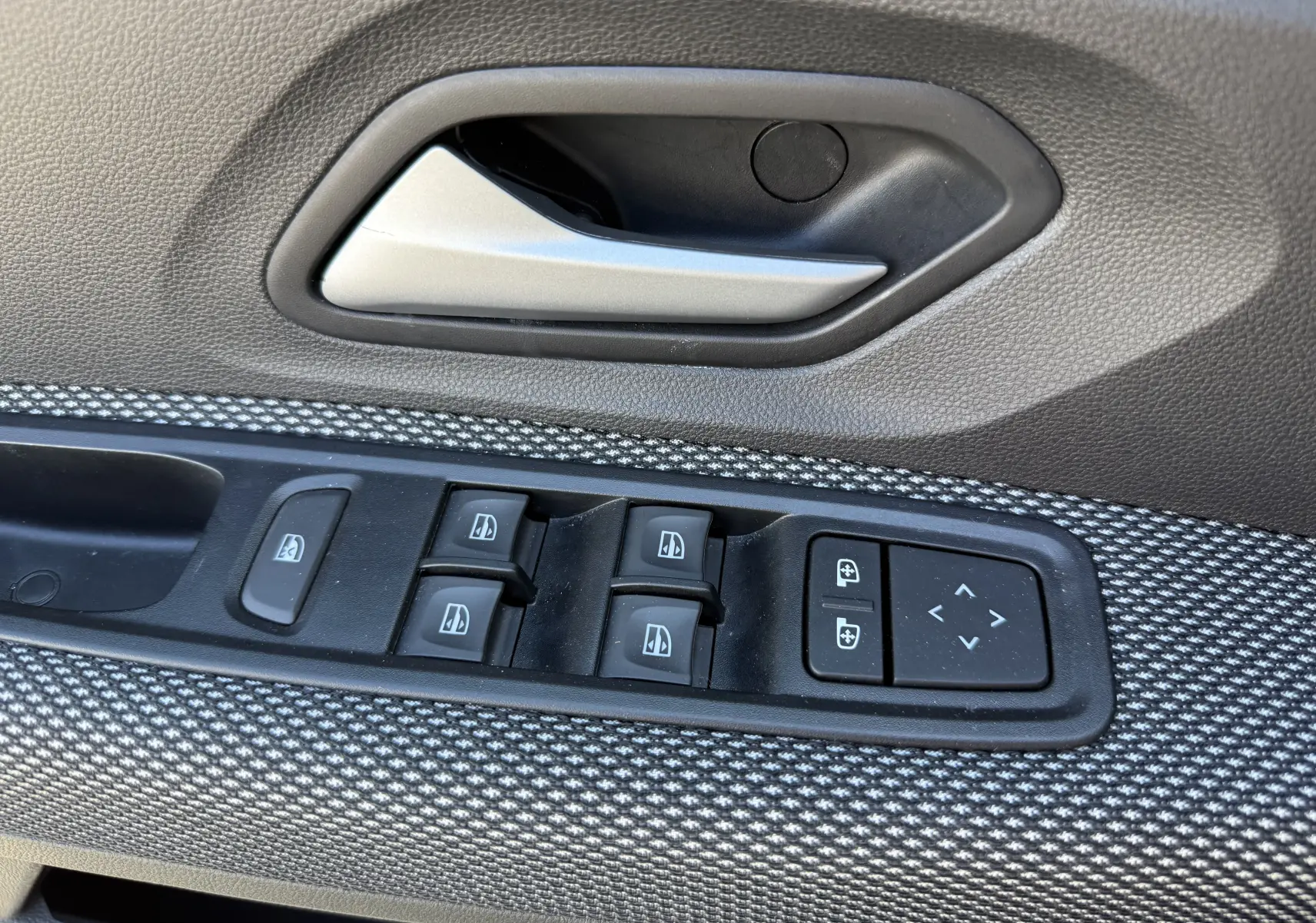 Gros plan sur la commande des vitres électriques et la poignée intérieure côté conducteur du Dacia Sandero Stepway 2025, finition tissu gris.