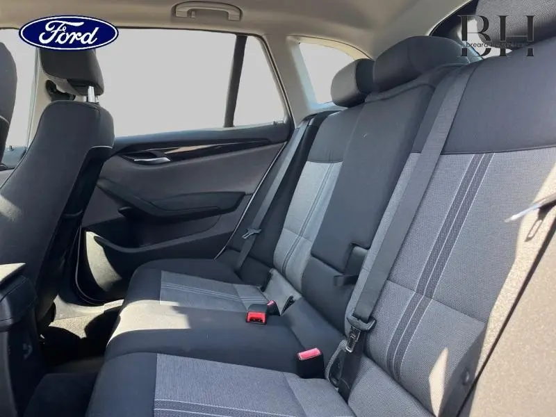 Vue intérieure des sièges arrière d'une BMW X1 gris, montrant la banquette 3 places avec ceintures de sécurité et appuie-têtes.