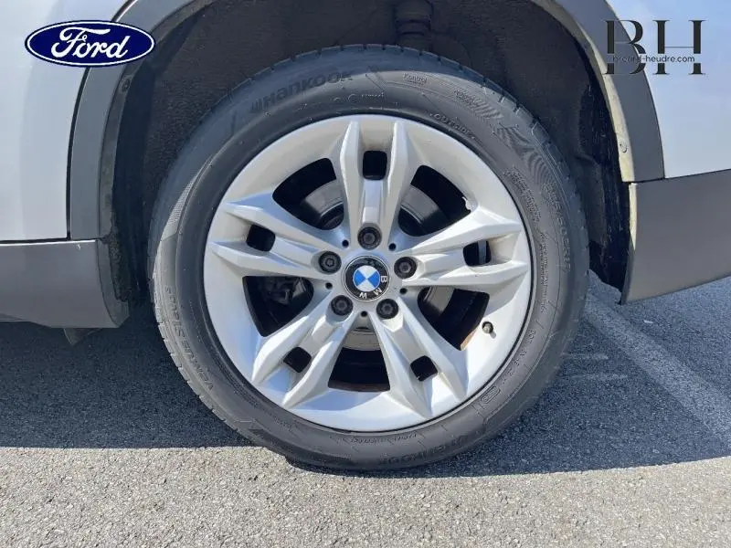 Gros plan sur la roue avant droite avec jante alu 17 pouces d’une BMW X1 gris métallisé, montrant le logo BMW au centre.