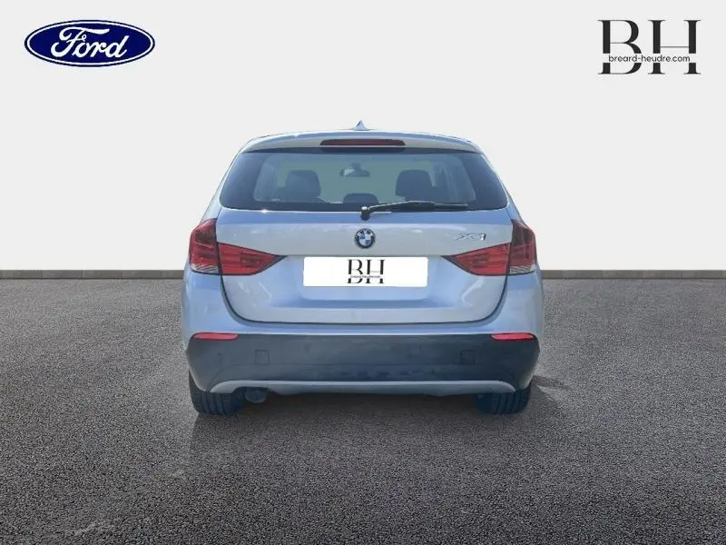 Vue arrière d’un BMW X1 gris métallisé de 2011 avec feux arrière rouges et logo BMW visible.