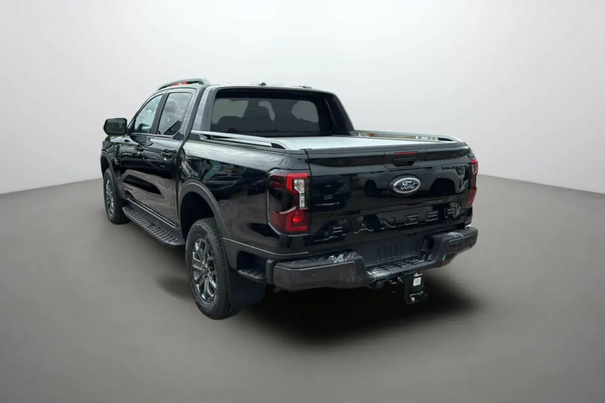Ford Ranger 2025 noir agate vu en 3/4 arrière droit, avec benne couverte et attelage visible.
