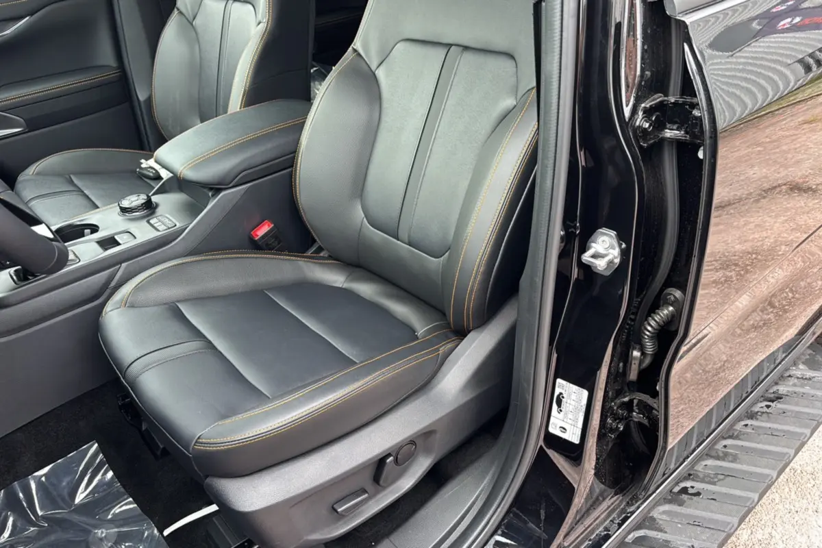 Vue intérieure côté conducteur du Ford Ranger 2025 noir agate, siège en cuir noir avec surpiqûres orange et console centrale visible.